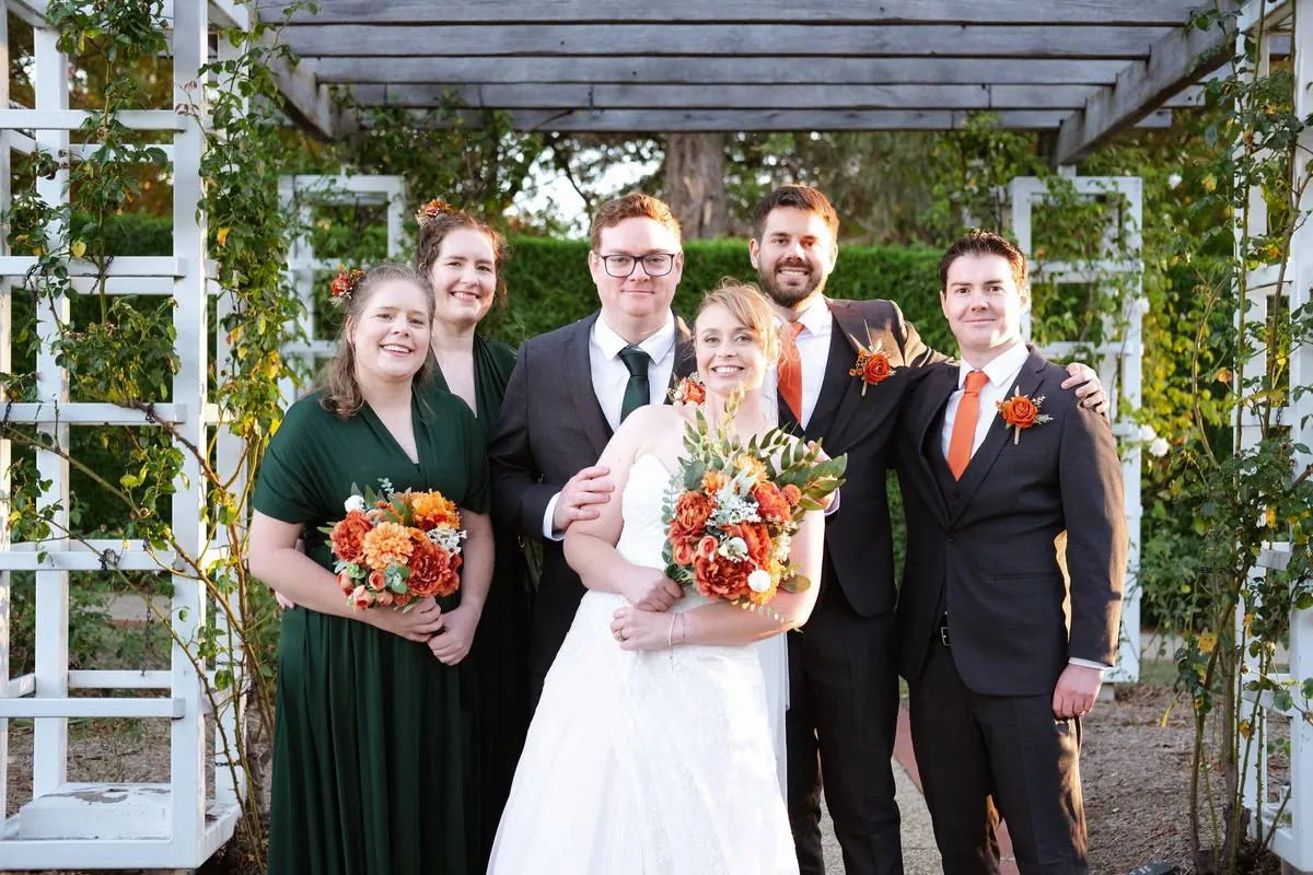 Bride and groom with wedding party under a garden arbour