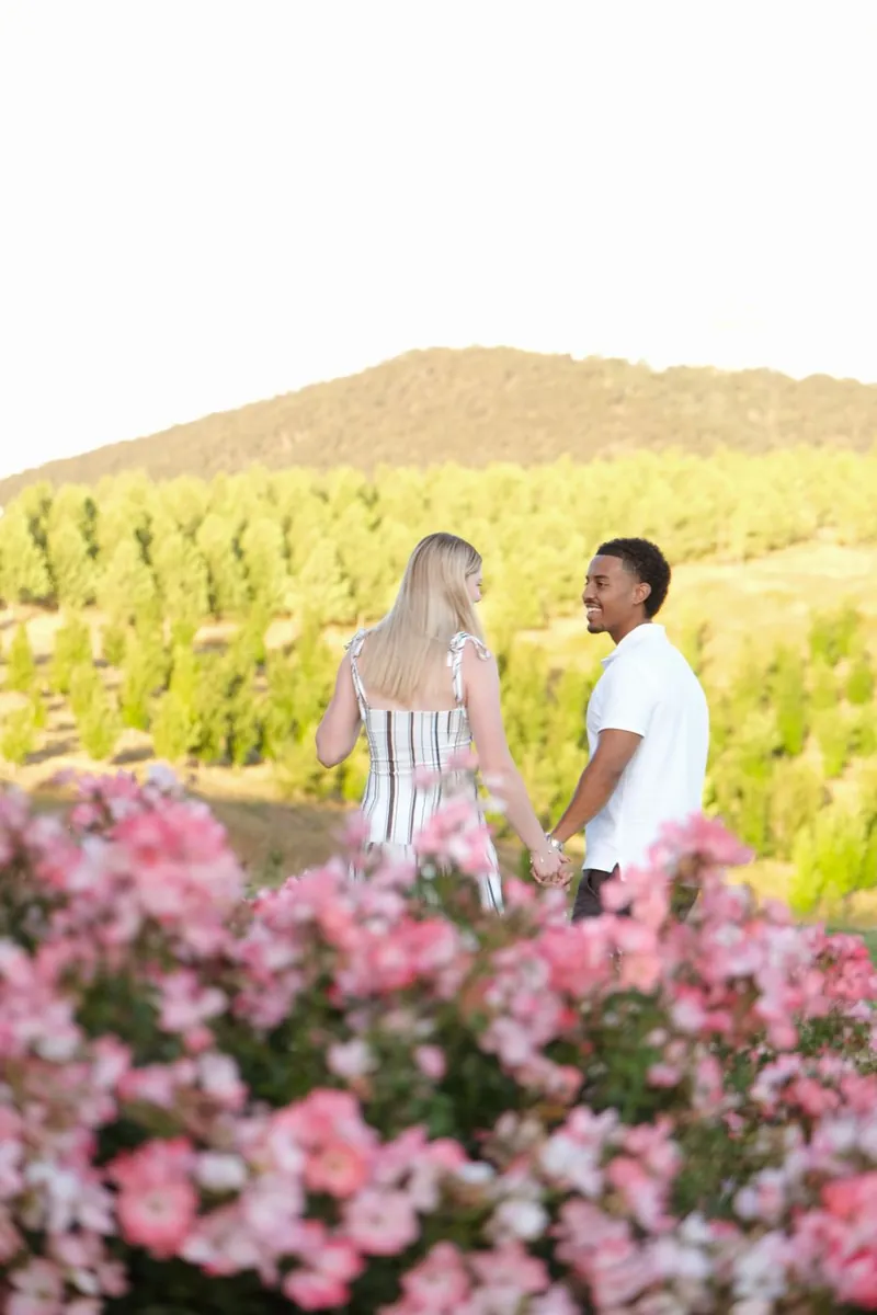 Couple holding hands walking through a pink flower garden