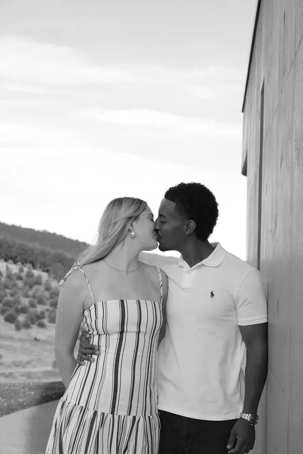 Couple kissing beside a building, black and white