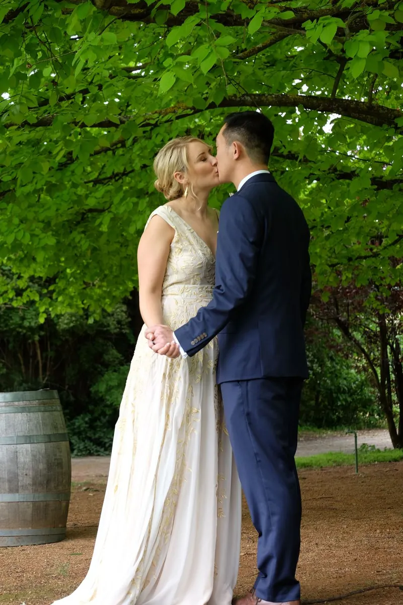 Couple kissing under a leafy arbour beside a wine barrel