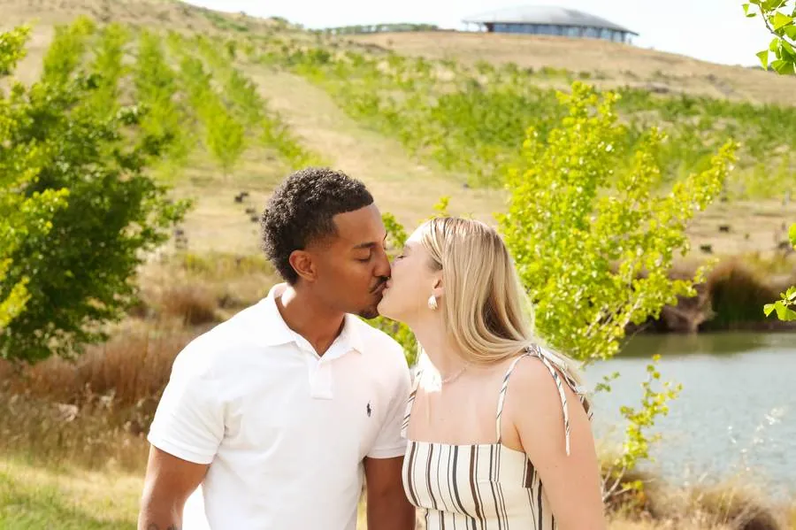 Engaged couple sharing a kiss in golden countryside light beside a lake