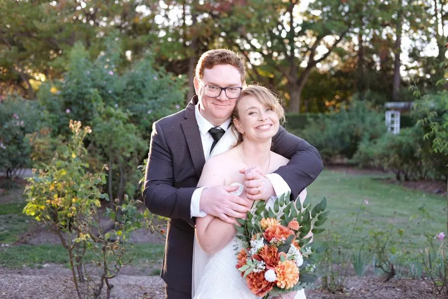 Groom holding bride close, both smiling in golden light