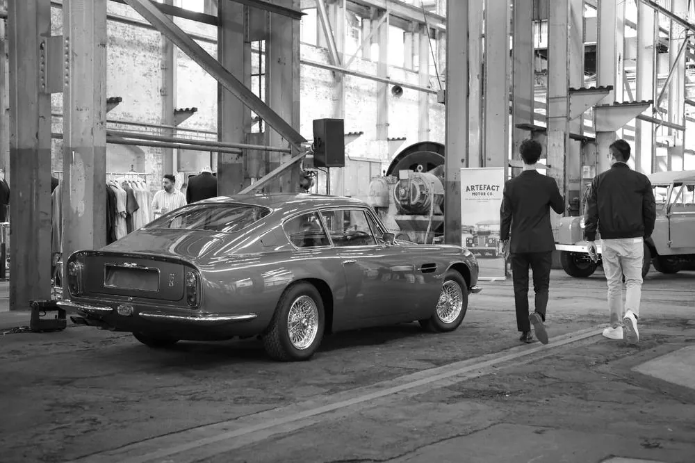 Guests walking past a vintage Aston Martin at a car event, black and white