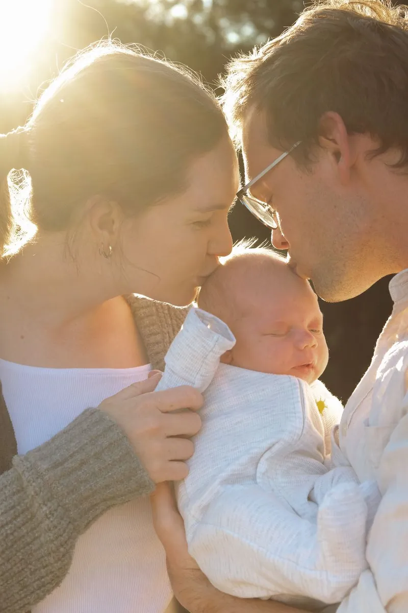 Parents kissing their newborn's head in golden hour light